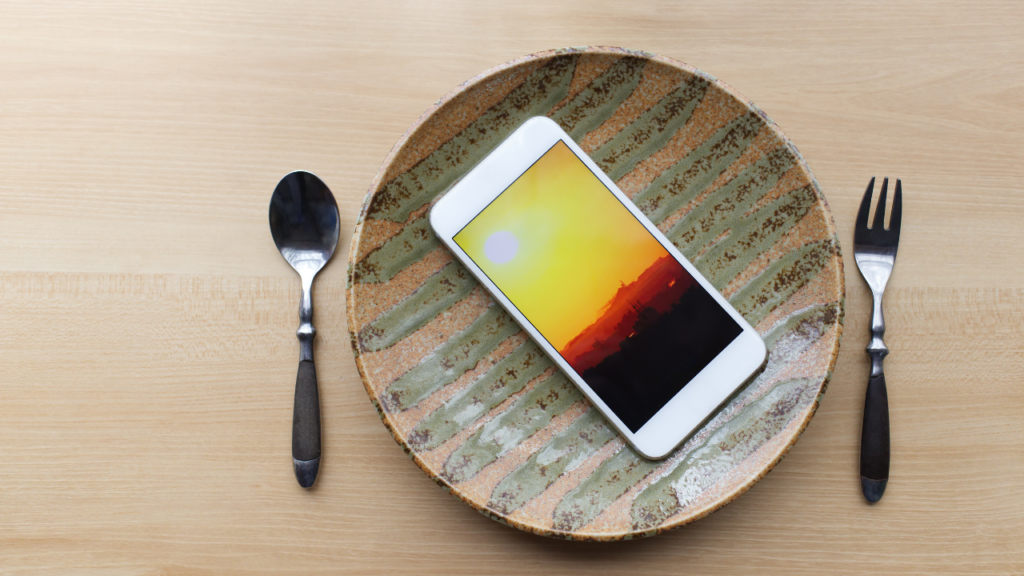 celular servido em prato de cerâmica com pintura abstrata ao lado de talheres de cabo preto em uma mesa de madeira